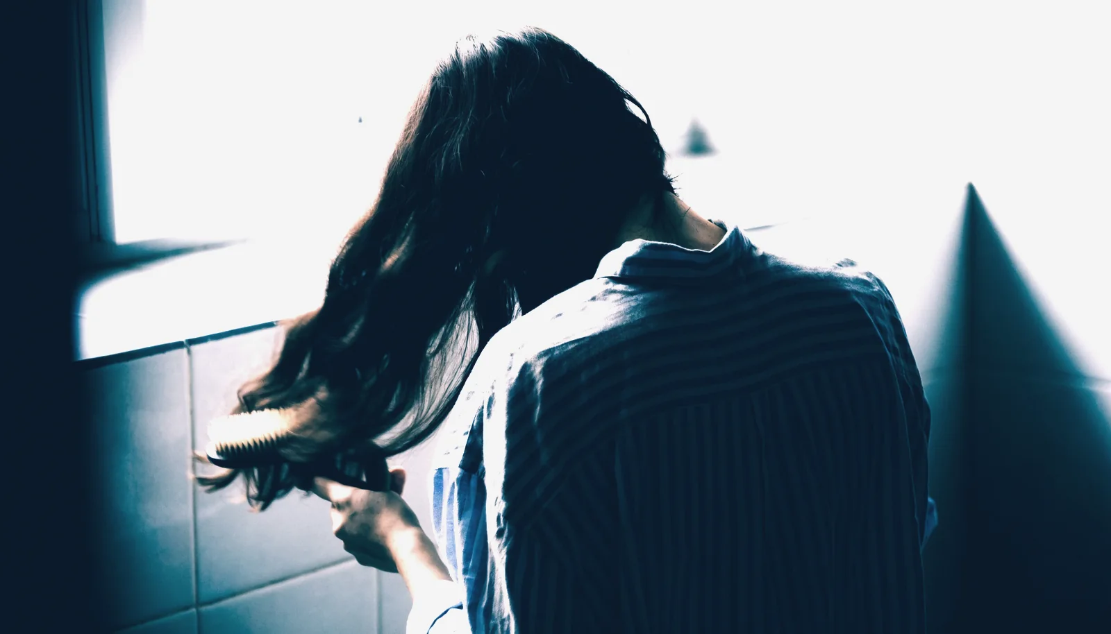 Caída del cabello 1 Péptidos en venta Mujer peinando su cabello largo junto a la ventana